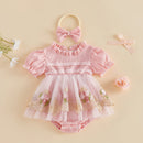 A baby girl's pink short-sleeve romper with a ruffled collar, lace trim, and a floral tulle skirt, shown with a matching pink bow headband on a beige background with decorative flowers, Obroi