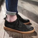 Black leather shoes with brown soles worn by a person on a wooden floor, Obroi