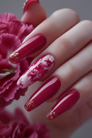 Hand with red and white floral nail design against a pink flower background, Obroi