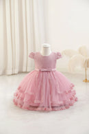 A pink toddler girl's party dress displayed on a white mannequin dress form. The dress features a textured honeycomb lace bodice, short puff sleeves, a matching pink satin waistband, and a tiered tulle skirt with lace trim, Obroi