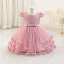 A pink toddler girl's party dress displayed on a white mannequin dress form. The dress features a textured honeycomb lace bodice, short puff sleeves, a matching pink satin waistband, and a tiered tulle skirt with lace trim, Obroi