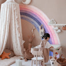 Child playing at a desk with a rainbow decoration on the wall, surrounded by soft furnishings and a dog, Obroi