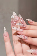 Hand with decorative nails featuring bows, cherries, and rhinestones on a neutral background, Obroi