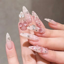 Hand with decorative nails featuring bows, cherries, and rhinestones on a neutral background, Obroi