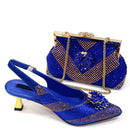 A royal blue embellished women's slingback heeled shoe with a matching beaded clutch handbag, both decorated with gold rhinestones and floral embellishments, set against a plain white background, Obroi