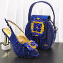 Blue high-heeled shoe and matching handbag with gemstone details on a white background, Obroi