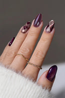 Close-up of a hand with maroon nail polish and gold rings on a neutral background, Obroi