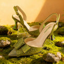 Green high-heeled shoes with rhinestone details on a mossy surface, Obroi