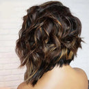 A woman shown from the back wearing a short, wavy wig with dark brown and warm blonde highlights. The brand logo 'Obroi' is visible in the top-left corner against a white brick wall background, Obroi