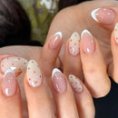 Close-up of hands with pink and white nail polish featuring small gold dots.