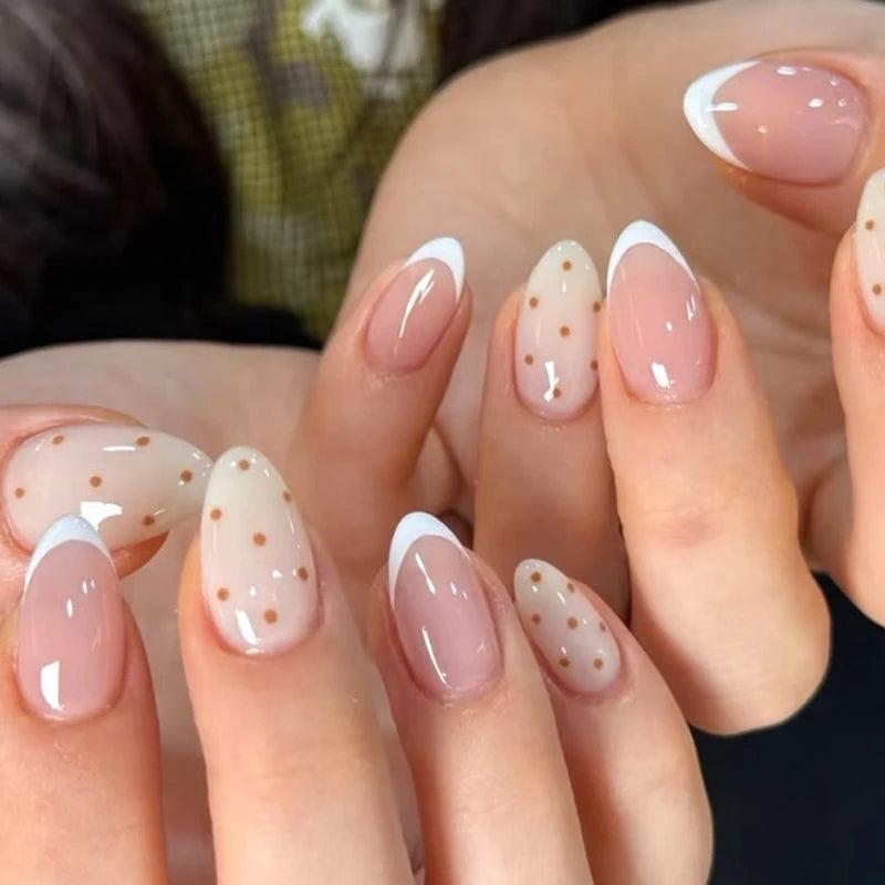 Close-up of hands with pink and white nail polish featuring small gold dots.