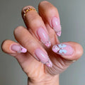 Hand with pink nail art featuring flowers and beads on a neutral background, Obroi