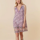 A sleeveless V-neck mini dress with a purple and pink floral pattern and a decorative border, modeled against a solid beige background, Obroi