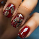 Close-up of a hand with red nail polish and leaf designs on a blurred background, Obroi