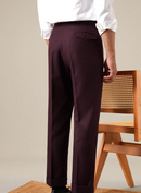 Person wearing maroon pants and a white shirt in front of a wooden chair, Obroi