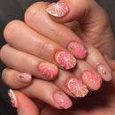 Hand with pink and orange floral nail art on a dark background, Obroi