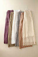 Five pairs of women's pants in different colors hanging on a rack against a light background, Obroi