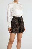A model wearing high-waisted leopard print shorts with a black drawstring waist, styled with a white satin long-sleeve blouse against a light gray studio background, Obroi