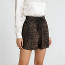 A model wearing high-waisted leopard print shorts with a black drawstring waist, styled with a white satin long-sleeve blouse against a light gray studio background, Obroi