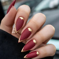 Hand with maroon nails featuring gold accents held against a blurred background, Obroi
