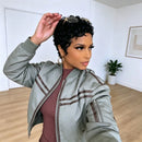 A woman wearing a light sage green bomber jacket with brown stripes over a burgundy ribbed top, posing in a bright room with light wood floors and white walls, Obroi