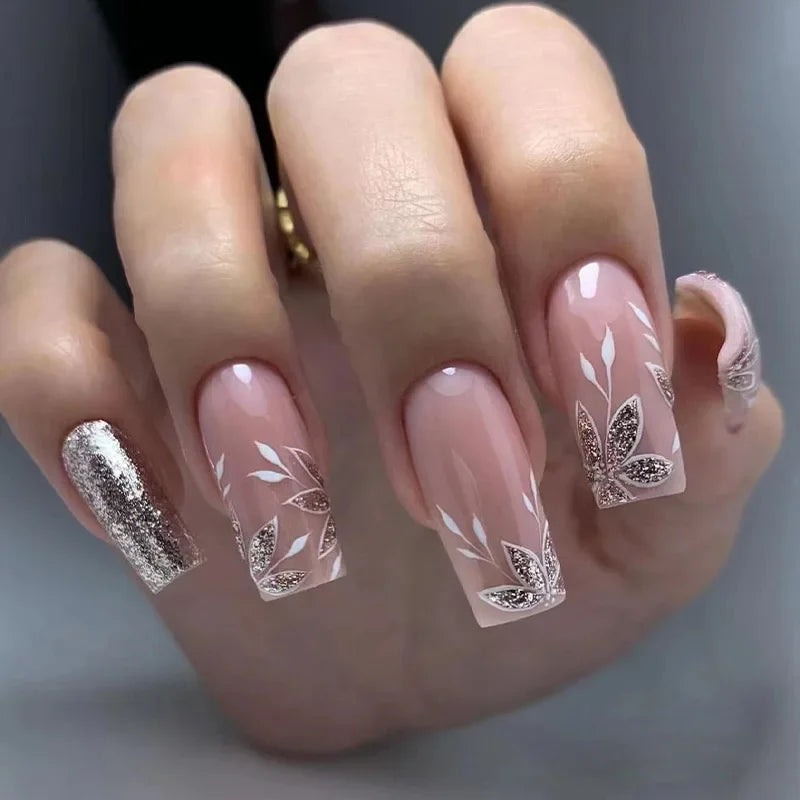Close-up of a hand with decorative nails featuring floral designs and glitter | obroi
