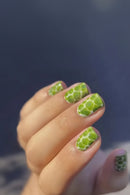 Close-up of a hand with green nail art on a blurred background, Obroi
