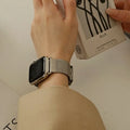 A close-up of a person's wrist wearing a silver mesh metal band attached to a smartwatch, while holding a white box labeled Obroi.
