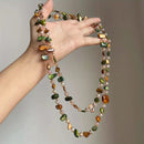 Hand holding a colorful beaded necklace against a neutral background, Obroi