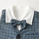 A close-up of a children's collared shirt or dress with a blue and gray plaid pattern, a white collar, and a matching plaid bow tie, shown against a plain light background, Obroi