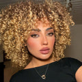 Woman with blonde curly hair wearing a black top indoors, Obroi
