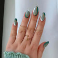 Hand with teal and gold nail design on a plain background, Obroi