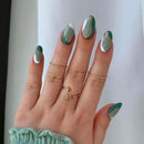 Hand with teal and gold nail design on a plain background, Obroi