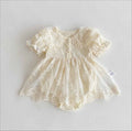 A cream-colored baby dress with delicate lace and floral embroidery, featuring short ruffled sleeves, a buttoned neckline, and a flared skirt, laid flat on a light gray background, Obroi