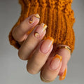 Close-up of a hand with orange and beige nail polish wearing a mustard yellow knitted sweater, Obroi