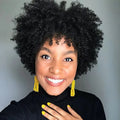 Woman with an afro wearing a black turtleneck and yellow earrings against a gray background, Obroi