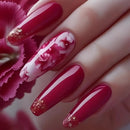 Hand with red and white floral nail design against a pink flower background, Obroi