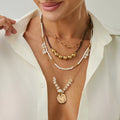 Woman wearing multiple necklaces with a plain background, Obroi