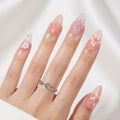 A close-up of a hand with long, glossy almond-shaped nails decorated with pink and white floral designs, wearing a silver twisted ring on a soft white background, Obroi