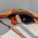 Open pouch with personal items including a phone, bottle, and lip balm on a textured white surface, Obroi
