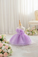 A lavender purple toddler girl's party dress displayed on a mannequin dress form. The dress features a strapless bodice with a large ruffled bow, a matching fabric waistband with a large fabric rose applique, and a tiered tulle skirt, Obroi
