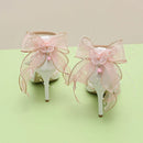 White high-heeled shoes with pink ribbons and decorative bows on a light green background, Obroi