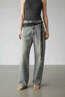Person wearing light blue jeans with a belt and fringe detail on a plain background, Obroi
