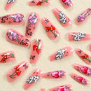 Decorative false nails with pink polish, red flowers, and black designs on a beige background, Obroi