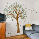 Living room with a large wall decal of a tree and birds, a gray sofa, and wooden cabinet, Obroi