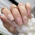 Obroi Close-up of a hand with pink nail art featuring a heart and snowflake design, wearing gold rings, against a blurred background.