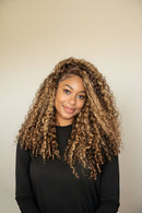 Woman with long, curly hair wearing a black top against a beige background, Obroi