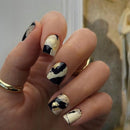 Obroi Hand with marbleized nail art featuring black, white, and gold on a neutral background