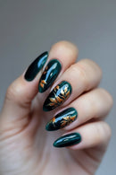Hand with dark green nails featuring gold leaf design on a neutral background, Obroi