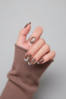 Hand with brown nail polish wearing a brown sleeve on a gray background, Obroi